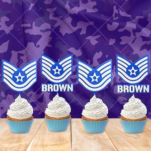 Peut inclure: Quatre cupcakes avec glaçage blanc et des paillettes bleues, chacun surmonté d'un insigne militaire bleu et blanc. Le mot "BROWN" est affiché entre les décorations de cupcakes. Les cupcakes sont dans des caissettes bleues sur une surface en bois.
