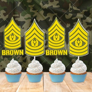 Puede incluir: Cuatro cupcakes con envoltorios azules y glaseado blanco, cubiertos con chispas azules. Cada uno tiene una insignia militar amarilla y verde en un palillo, con la palabra "BROWN" en amarillo.