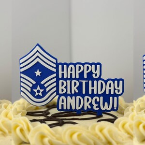 May include: A birthday cake with white frosting and chocolate swirls, topped with a blue and white cake topper. The topper features a military rank insignia and the words "HAPPY BIRTHDAY ANDREW!"