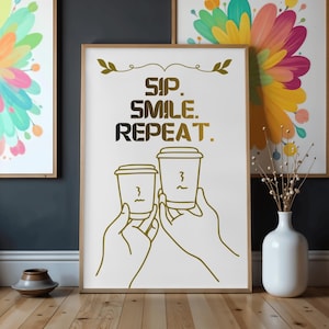 Puede incluir: Una impresión enmarcada con el texto dorado "SIP. SMILE. REPEAT." y dos tazas de café. La obra de arte está sobre un fondo blanco, con un marco de madera clara. La imagen tiene un diseño simple y moderno.