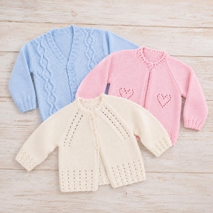 May include: Three knitted cardigans in light blue, soft pink, and cream. The blue cardigan features a cable knit pattern and buttons. The pink cardigan has heart-shaped cutouts and a button closure. The cream cardigan has eyelet details.
