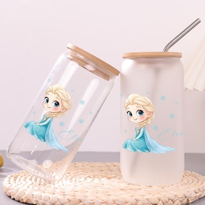 May include: Two glass tumblers with bamboo lids, one clear and one frosted, each featuring a cartoon illustration of a blonde character in a blue dress with snowflakes and the name Elsa written in cursive script, plus a metal straw.