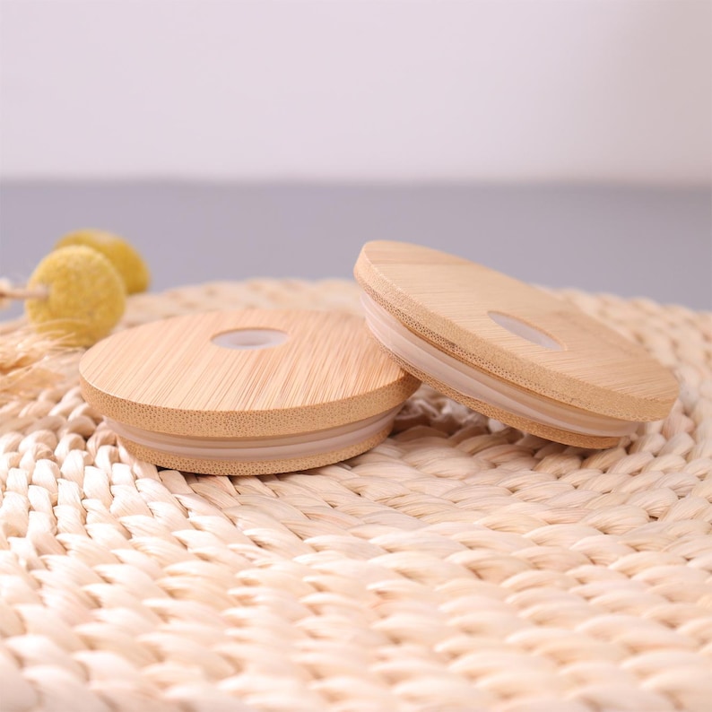 May include: Two circular bamboo lids for drinkware, each featuring a smooth, light-toned wood grain finish and a central circular opening. A translucent silicone gasket is fitted around the underside edge of each lid to ensure a secure seal.