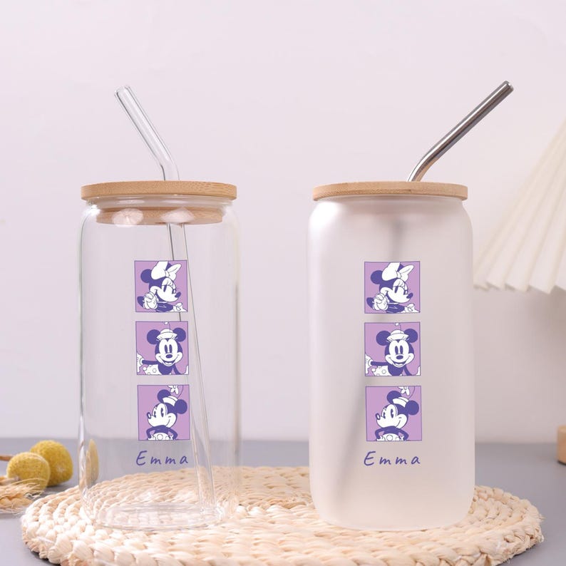 Puede incluir: Dos vasos de vidrio con tapas de bamb&uacute; y pajitas. Uno es transparente, el otro es esmerilado. Cada uno presenta un gr&aacute;fico vertical de tres cuadrados morados con personajes de rat&oacute;n y el nombre Emma en cursiva bajo el dise&ntilde;o.