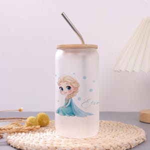 May include: A frosted glass tumbler with a bamboo lid and a bent metal straw. The tumbler features a cartoon illustration of a blonde character in a blue dress with the name Elsa written in cursive script and small blue snowflake accents.