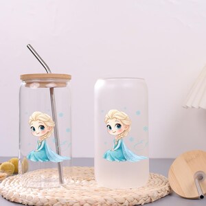 May include: Two glass tumblers with a cartoon illustration of a blonde character in a blue dress surrounded by small blue snowflakes. One tumbler is clear glass with a bamboo lid and metal straw, while the other is a frosted glass tumbler.