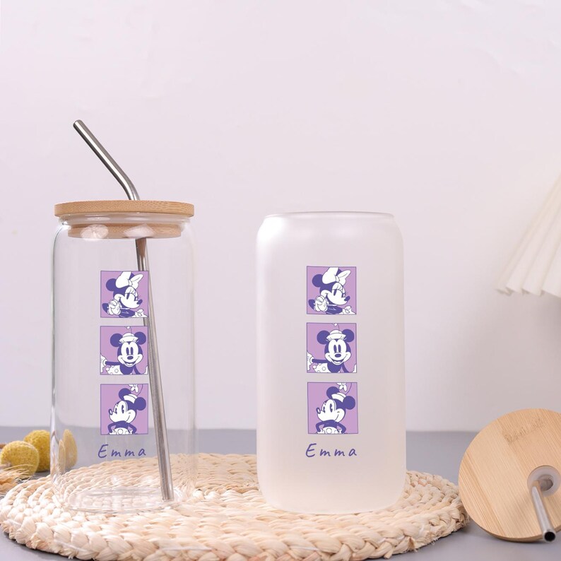 Puede incluir: Dos vasos de cristal, uno transparente y otro esmerilado, con tres gr&aacute;ficos cuadrados morados apilados de un rat&oacute;n de dibujos animados y el nombre Emma en azul. Ambos vasos incluyen una tapa de bamb&uacute; y una pajita de metal.