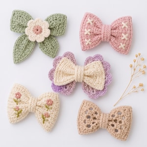 Pode incluir: Cinco laços de cabelo feitos à mão em crochê com vários designs. Um é verde sálvia com uma flor creme, um é rosa antigo com costuras em cruz brancas, um é creme com bordas festonadas roxas, um é creme com flores bordadas e um é renda bege.