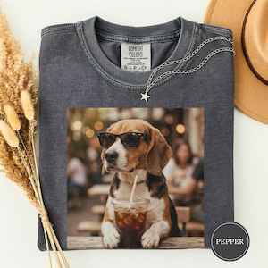 Könnte beinhalten: Ein anthrazitfarbenes T-Shirt mit Rundhalsausschnitt und einem Grafikdruck eines Beagle-Hundes, der eine schwarze Sonnenbrille trägt und einen Plastikbecher mit Strohhalm hält. Am Kragen befindet sich ein Comfort Colors-Etikett.