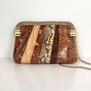 Puede incluir: Un bolso de mano vintage con un diseño de patchwork. El bolso presenta una mezcla de paneles marrones, beige y con estampado de piel de serpiente. Tiene un cierre dorado y una delicada correa de cadena. El estilo general es retro y elegante.