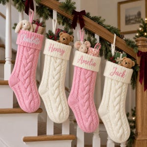 May include: Four cable-knit Christmas stockings in alternating pink and cream colours, each featuring a folded cuff embroidered with the names Charlotte, Henry, Amelia, and Jack. Each stocking contains a small plush animal and a gift box.