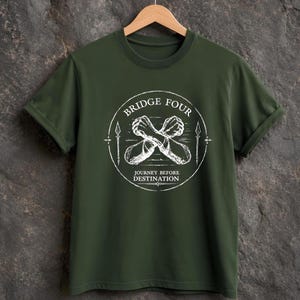 Puede incluir: Una camiseta de manga corta color verde oliva con un gráfico circular blanco en el pecho. El diseño muestra dos brazos cruzados con grilletes rotos, flanqueados por lanzas, con el texto BRIDGE FOUR y JOURNEY BEFORE DESTINATION.