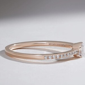 May include: Rose gold ring with a rectangular diamond and small accent diamonds set along the band. The ring is shown in a side view, highlighting the details of the setting and the sparkle of the stones.
