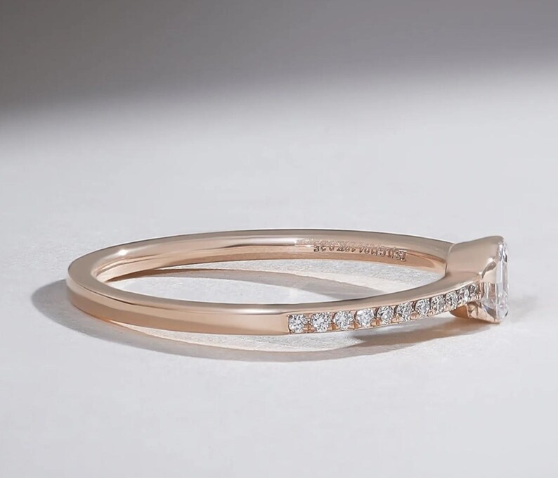 May include: Rose gold ring with a rectangular diamond and small accent diamonds set along the band. The ring is shown in a side view, highlighting the details of the setting and the sparkle of the stones.
