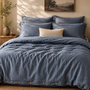 Peut inclure: Une parure de lit bleue avec une finition en tissu texturé et une rangée de boutons clairs le long du bord inférieur. L'ensemble comprend deux taies d'oreiller bleues assorties et un coussin décoratif rectangulaire beige au centre.