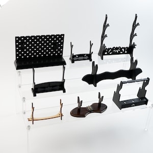 Può includere: Una collezione di espositori in legno di vari design e dimensioni. Gli espositori sono principalmente neri, alcuni con intricati motivi intagliati. Un espositore è marrone chiaro. Gli espositori sono disposti su ripiani in acrilico trasparente.