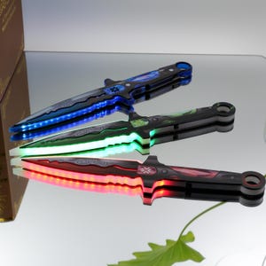 May include: Three decorative knives with illuminated blades in blue, green, and red. The knives have black handles and intricate designs on the blades. The blades are lit with LED lights, creating a vibrant glow.