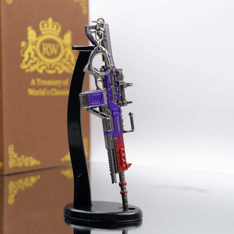 Puede incluir: Una r&eacute;plica en miniatura y detallada de un rifle, con un esquema de color p&uacute;rpura y rojo. El modelo incluye un llavero y est&aacute; montado en un soporte de exhibici&oacute;n negro. El dise&ntilde;o incorpora detalles intrincados, lo que sugiere un art&iacute;culo de colecci&oacute;n o novedad.