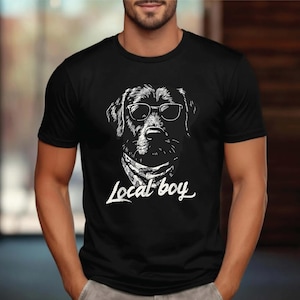 May include: Black t-shirt featuring a detailed white illustration of a dog wearing sunglasses and a bandana. The text "Local boy" is written in a stylish font below the dog's image. The shirt is a classic crew neck.