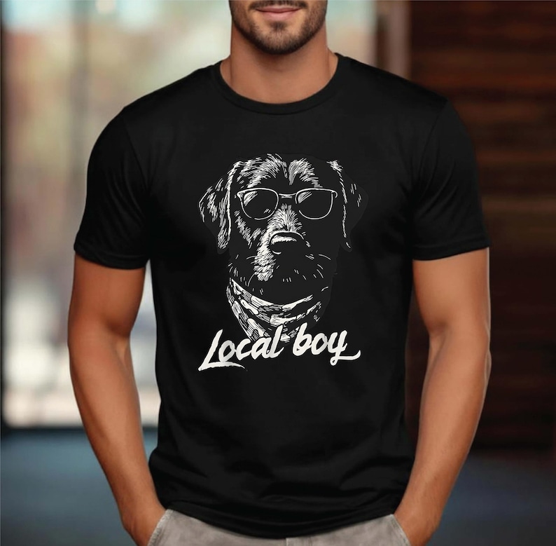 May include: Black t-shirt featuring a detailed white illustration of a dog wearing sunglasses and a bandana. The text "Local boy" is written in a stylish font below the dog's image. The shirt is a classic crew neck.
