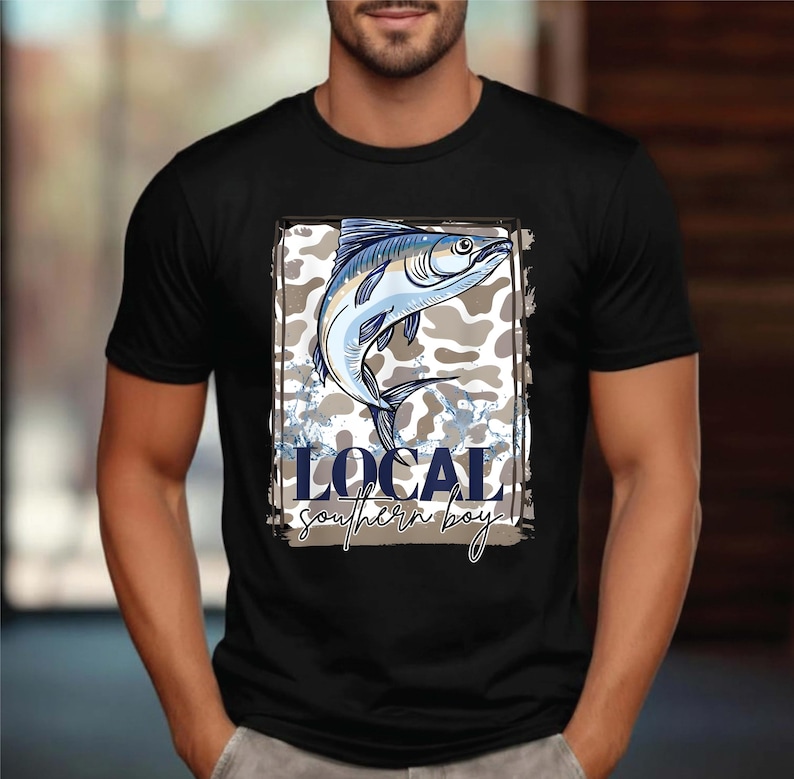 May include: Black t-shirt featuring a detailed illustration of a fish in shades of blue and white, set against a camouflage background. The text "LOCAL southern boy" is displayed below the fish in a stylized font.