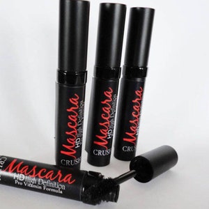 May include: Four black mascara tubes with red text that reads "Mascara HD High Definition Pro Vitamin Formula". One tube is open, revealing the brush. The mascara tubes are arranged on a white surface.