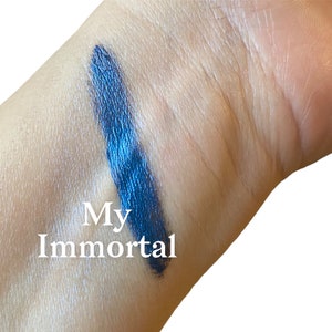 May include: A close-up of a blue eyeshadow swatch on a person's arm. The swatch is labelled "My Immortal".