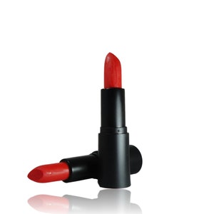 May include: A vibrant red lipstick in a matte black cylindrical tube. One lipstick stands upright with the cap removed, revealing the bright red pigment, while a second identical lipstick lies horizontally at its base on a white surface.