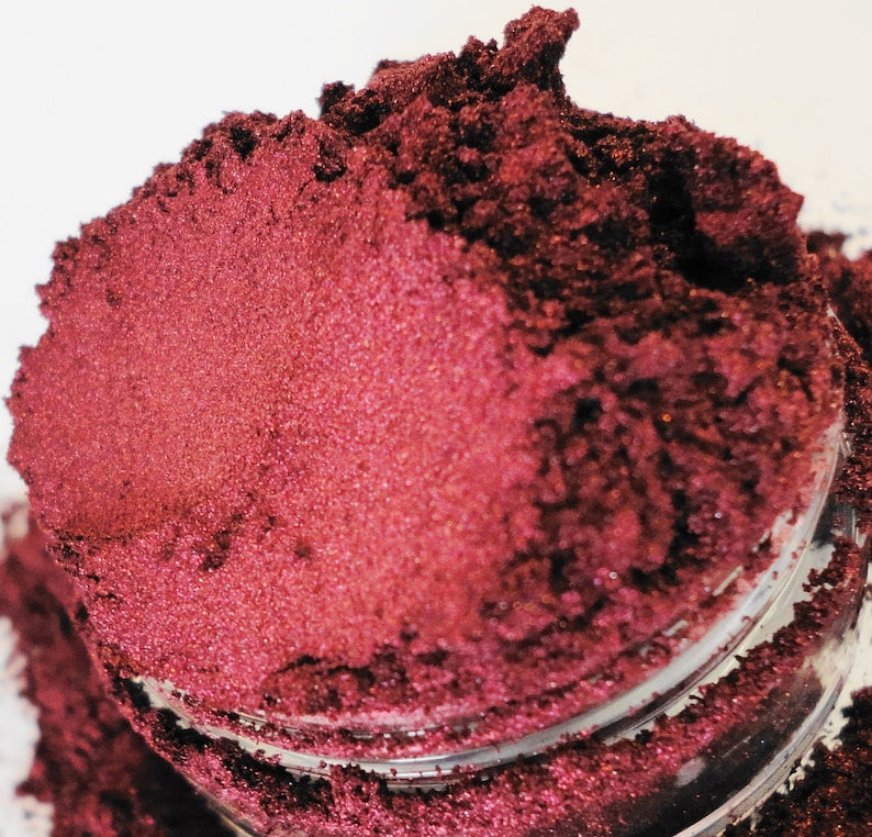 May include: A close-up of a deep red mica powder with a shimmery finish. The powder is in a small glass jar.