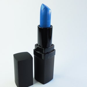 May include: A lipstick in a black rectangular tube with a matching removable cap. The lipstick bullet is a vibrant, metallic blue color with a slanted tip, extending upward from the black plastic casing, which features a square base design.