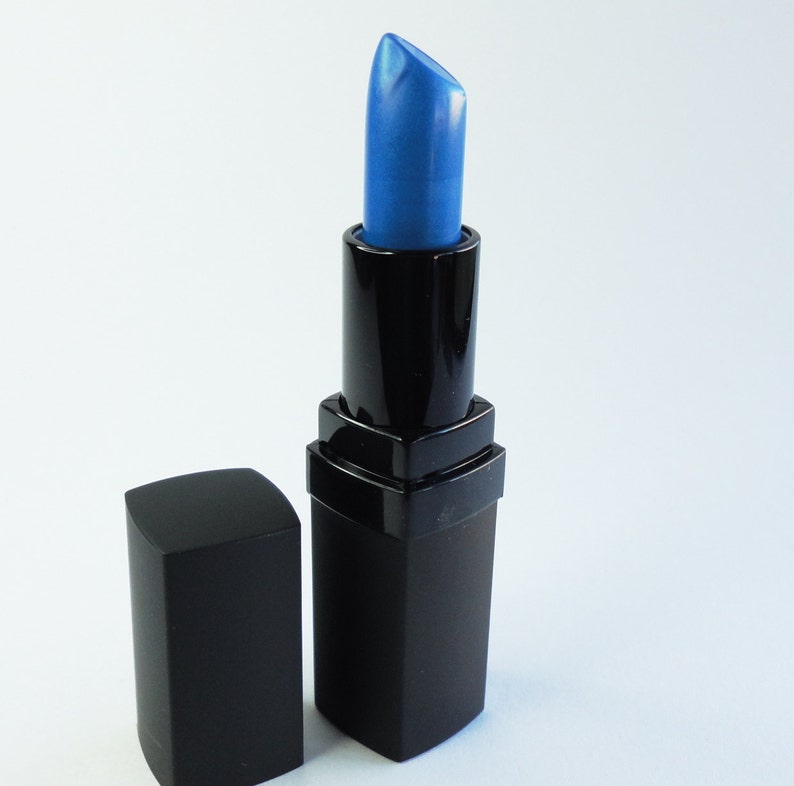 May include: A lipstick in a black rectangular tube with a matching removable cap. The lipstick bullet is a vibrant, metallic blue color with a slanted tip, extending upward from the black plastic casing, which features a square base design.