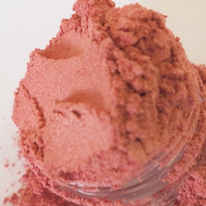 May include: A close-up of a pile of loose, fine, shimmery, pink cosmetic pigment powder.