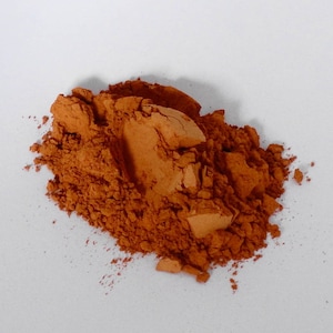 May include: A pile of loose, orange-brown powder. The powder is finely ground and has a slightly rough texture.