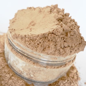 May include: A glass jar filled with a light brown powder. The powder is spilling out of the jar onto a white surface.