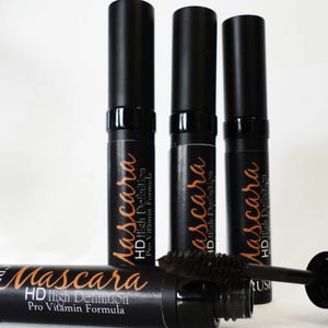 May include: Black mascara tubes with the text "Mascara HD High Definition Pro Vitamin Formula" in a copper color. One tube has the brush extended. The mascara tubes are on a white background.