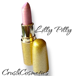 Könnte beinhalten: Ein Lippenstift in einem schimmernden Hellrosa, untergebracht in einer mit goldenem Glitzer überzogenen Hülse mit passender Kappe. Der Text Lilly Pilly ist in schwarzer Schreibschrift gedruckt, darunter steht der Text CrushCosmetics.
