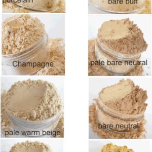 May include: Six small glass jars filled with different shades of beige powder. The jars are labeled with the names of the powder shades: porcelain, bare buff, champagne, pale bare neutral, pale warm beige, bare neutral, warm beige, and honey beige.