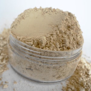 May include: A clear glass jar filled with a light brown powder. The powder is loose and has a slightly grainy texture.