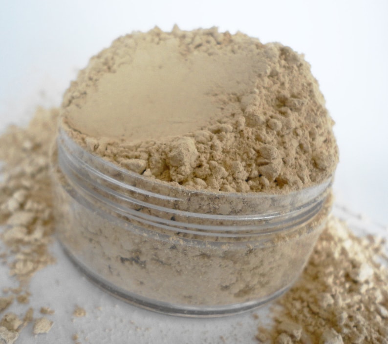 May include: A clear glass jar filled with a light brown powder. The powder is loose and has a slightly grainy texture.