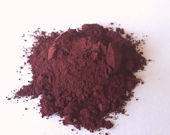 May include: A pile of dark red powder on a white surface. The powder is finely ground and has a smooth texture.