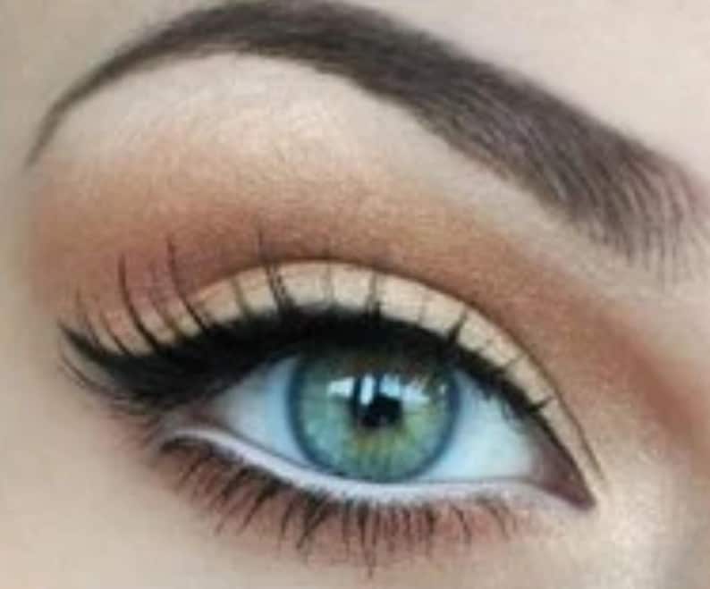 May include: Close-up of an eye with teal iris, dark lashes, and a defined brow. The eye makeup includes a black eyeliner and a light brown eyeshadow. The skin around the eye is a light peach color.