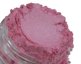 May include: A clear plastic jar filled with loose, shimmering pink cosmetic pigment powder. The fine, metallic-finish powder is piled high above the rim of the container, displaying a vibrant, light-reflecting texture with a soft, pearlescent sheen.