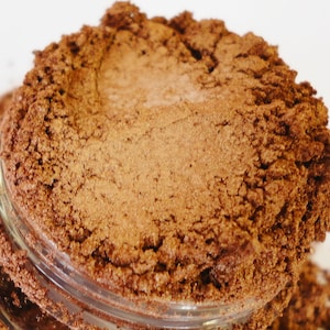 May include: Close-up of a jar of brown mica powder with a shimmery finish.