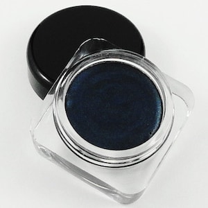 Könnte beinhalten: Ein kleiner, runder Behälter mit dunkelblauem Creme-Lidschatten und einem schwarzen Deckel.