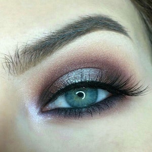 Op de afbeelding: Close-up van een blauw oog met zilveren en bruine oogschaduw, zwarte eyeliner en lange zwarte wimpers.