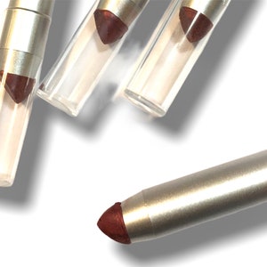 Puede incluir: Cuatro lápices de ojos plateados y marrones con punta afilada. Los lápices están en tubos de plástico transparente.