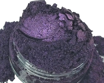 May include: A close-up of a small jar of purple iridescent mica powder. The powder is a fine, shimmery texture and has a deep, rich color.