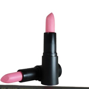 May include: Two lipstick tubes with matte black cylindrical casings. One tube stands vertically with the light pink lipstick bullet extended, while the second tube lies horizontally at the base with its light pink lipstick bullet partially exposed.