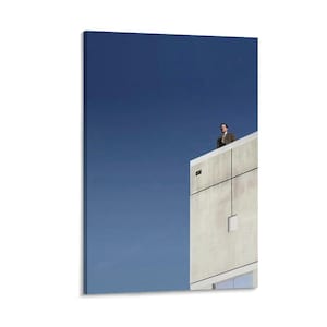 May include: A canvas print featuring a man in a suit standing on the edge of a building against a clear blue sky. The building is a light beige color with a minimalist design. The artwork has a modern, architectural theme.