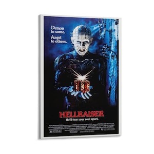 May include: A framed movie poster for the horror film "Hellraiser." The poster features a dark blue background with the character Pinhead holding a puzzle box. Text includes "Demon to some. Angel to others." and "He'll tear your soul apart."